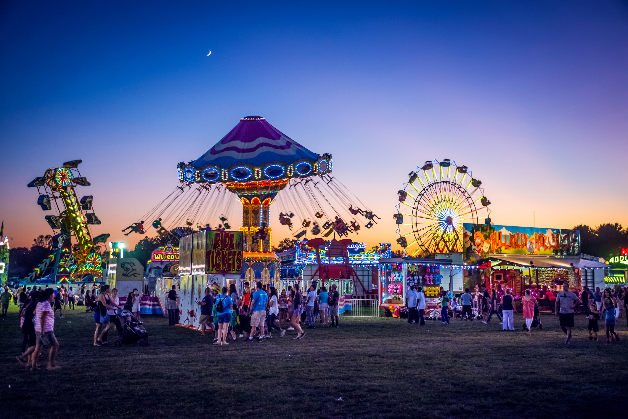 Wide shot of lighted carnival rides silhouetted against a dusk sky